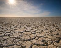 blue sky with sun setting over cracked dry land