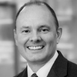 Black and white headshot of a man in a suit and tie smiling