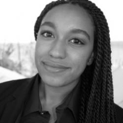A Black woman with braids in a blazer smiles at the camera
