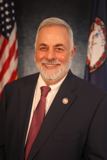 Mike smiling for a headshot with the U.S and Virginia flags behind hi,.
