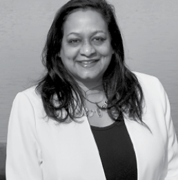  Radhika Fox smiling at the camera and wearing a white blazer and black shirt