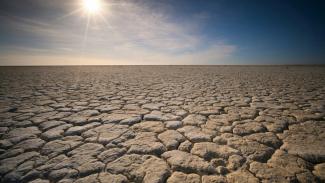 blue sky with sun setting over cracked dry land